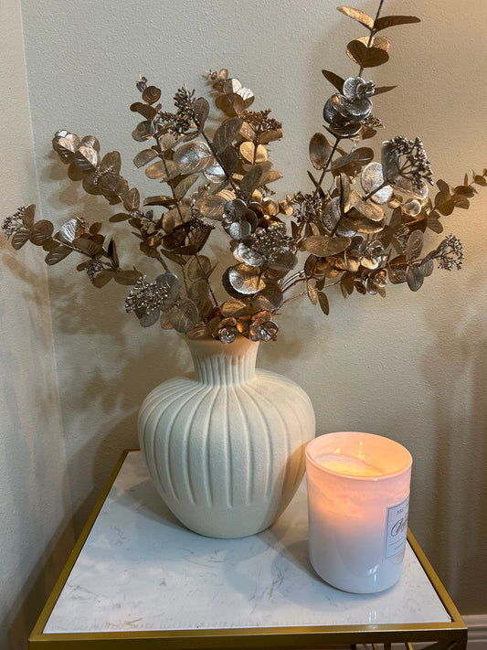Un florero blanco moderno, decorativo un follaje de flores dorada, con una vela blanca grande, decorativo, cerámica grueso